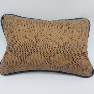 Könnte beinhalten: Ein braunes Kissen mit Schlangenhautmuster und schwarzem Besatz.