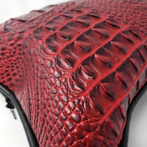 Puede incluir: Bolso de cuero rojo con estampado de cocodrilo, con cremallera y ribetes negros.