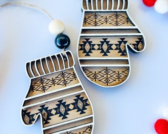May include: Two wooden ornaments shaped like mittens with a brown and black geometric pattern. The ornaments are strung on a white and brown beaded garland.