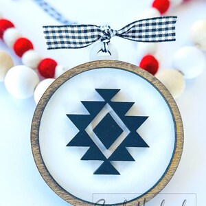 May include: A round wooden ornament with a white background and a black geometric design. The ornament has a black and white checkered ribbon attached to it.