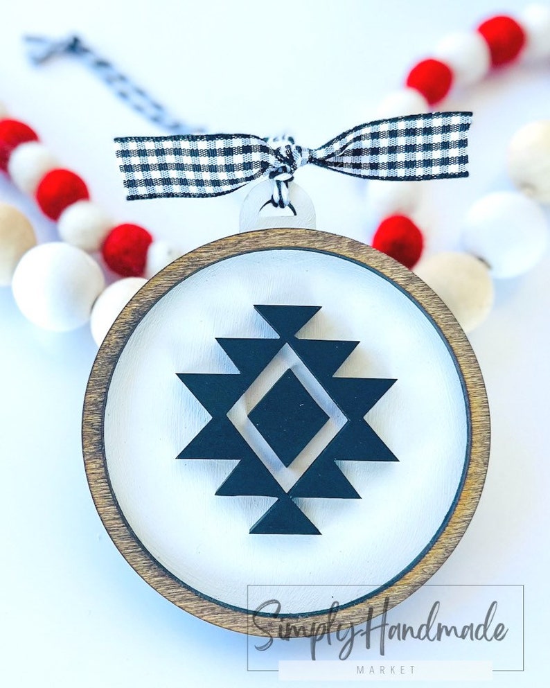 May include: A round wooden ornament with a white background and a black geometric design. The ornament has a black and white checkered ribbon attached to it.