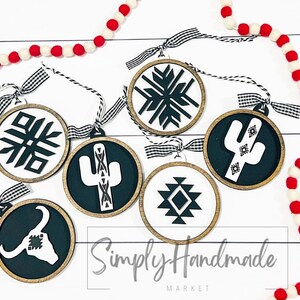May include: Six round wooden ornaments with black and white geometric designs. The designs include a snowflake, a cactus, a diamond pattern, and a bull's head. The ornaments are hanging from black and white checkered ribbon. The text "Simply Handmade Market" is visible at the bottom of the image.