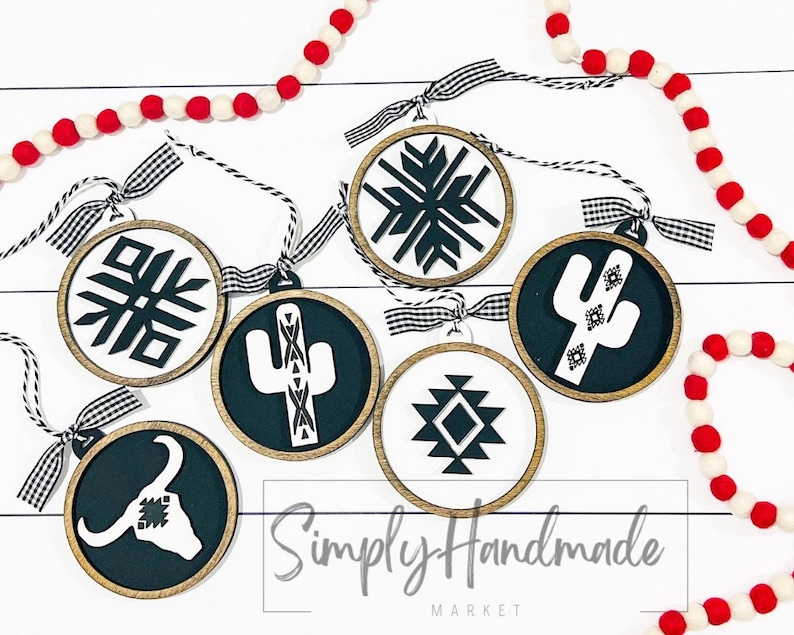 May include: Six round wooden ornaments with black and white geometric designs. The designs include a snowflake, a cactus, a diamond pattern, and a bull's head. The ornaments are hanging from black and white checkered ribbon. The text "Simply Handmade Market" is visible at the bottom of the image.