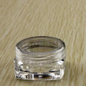 May include: A clear, square-shaped plastic container with a lid. The container is empty and has a smooth, shiny surface.