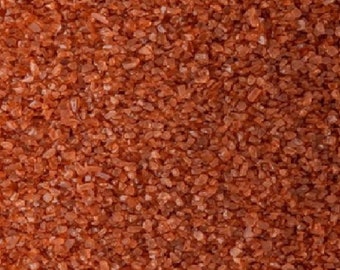 May include: Close-up of red Himalayan salt crystals. The salt is a fine grain and has a reddish-brown color.