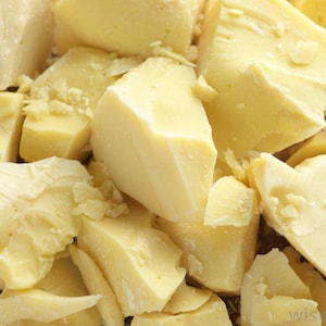 Puede incluir: Primer plano de trozos rotos de manteca de karité cruda, sin refinar, de color amarillo pálido.