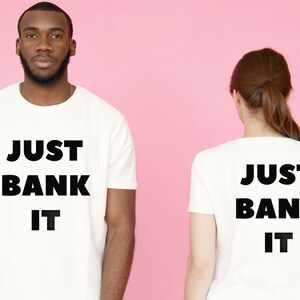 May include: Two white t-shirts with the text "JUST BANK IT" printed on them. One shirt has the text on the front and the other has the text on the back.
