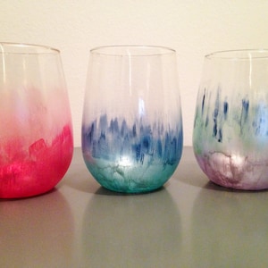 Op de afbeelding: Drie heldere glazen wijnglazen met een gradiënt ombre-effect. De glazen zijn geschilderd in roze, blauwe en paarse tinten.