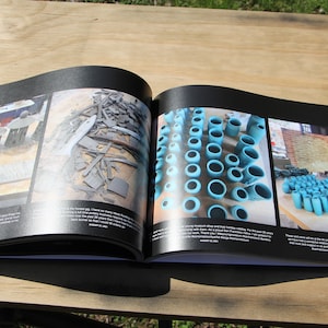 May include: An open book with three photos of ceramic pottery. The first photo shows a group of small, gray ceramic pots. The second photo shows a pile of gray ceramic shards. The third photo shows a collection of blue ceramic mugs.