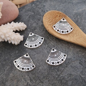 May include: Four silver metal half-circle charms with a geometric design. The charms have a raised, textured pattern and a smooth, shiny finish.