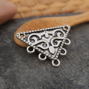 May include: Silver triangle pendant with an ornate design and five jump rings. The pendant features a filigree pattern and is ideal for adding a touch of elegance to jewellery projects.