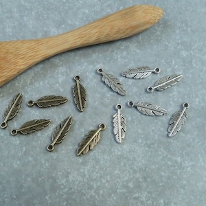 May include: A collection of silver and bronze feather charms with a hole at the top for attaching to jewellery or other crafts.