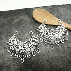 Peut inclure: Deux breloques pendantes en métal argenté avec des motifs floraux complexes. Chaque breloque a une forme de croissant avec cinq boucles pendantes.