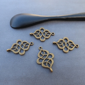 May include: Four antique gold metal charms with intricate designs. Each charm features a repeating pattern of interlocked loops and curves.