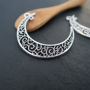 May include: Two silver filigree crescent moon charms with a decorative swirl design.