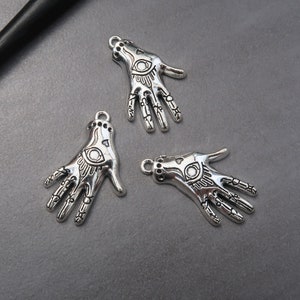May include: Three silver charm pendants in the shape of a hand with an eye in the palm. The charms are detailed with lines and patterns.