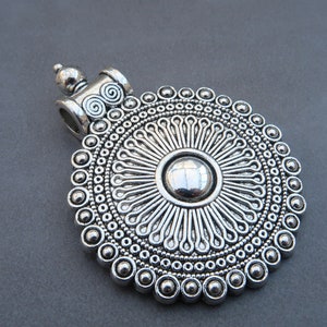 Peut inclure: Pendentif en argent avec un motif circulaire présentant un motif central en forme de soleil entouré de cercles concentriques de perles.
