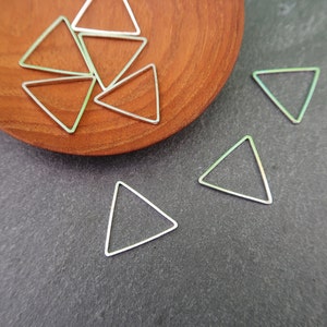 May include: A close-up of silver triangle jump rings on a wooden surface. The jump rings are arranged in a random pattern.