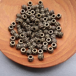 Op de afbeelding: Een stapel antieke gouden metalen kralen met een getextureerd oppervlak. De kralen bevinden zich in een houten kom.