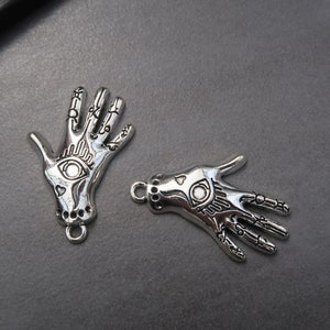 May include: Two silver charm pendants in the shape of a hand with an eye design. The charms have a detailed design and are perfect for jewelry making.
