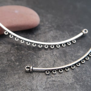 May include: Two silver metal curved jewelry connectors with small round beads along the edge. The connectors have a loop at each end.