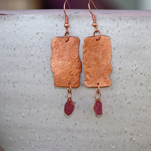 May include: Copper earrings with a hammered texture and a dangling pink gemstone.