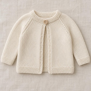 Könnte beinhalten: Eine cremefarbene Strickjacke mit langen Ärmeln, einem Rundhalsausschnitt und einem einzelnen Holzknopfverschluss am oberen Rand. Das Kleidungsstück ist mit einer kraus rechts gestrickten Textur an Kragen, Bündchen, Saum und Knopfleiste versehen.