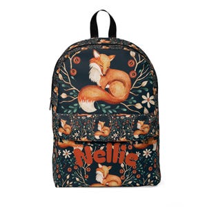 May include: A dark navy blue backpack featuring a repeating pattern of orange foxes, white flowers, and green foliage. The front pocket displays the name Nellie in large, bold, orange letters. The bag has a top handle and a zippered main compartment.