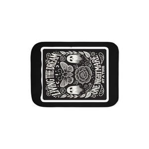 May include: Black and white decorative coaster with a rectangular design. The coaster features a floral and insect illustration with the phrases "LIVING THE DREAM" and "ONE NIGHTMARE AT A TIME".