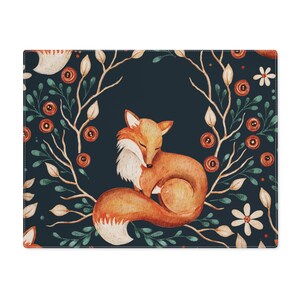 Peut inclure: Un set de table rectangulaire avec une illustration à l'aquarelle d'un renard endormi. Le renard est orange et blanc, recroquevillé. Le fond est bleu foncé avec des accents floraux et de feuilles orange, verts et blancs.