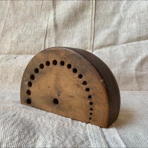 May include: A wooden half-circle bead board with a row of holes around the edge. The board is made of dark wood and has a natural finish.