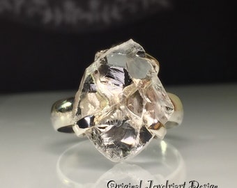 May include: A silver ring with a large, clear, faceted crystal set in the center. The crystal is rough and has a natural, raw look.