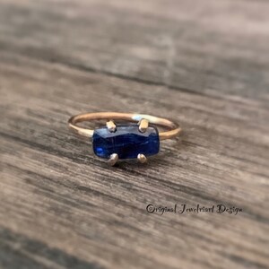 May include: A gold ring with a dark blue rectangular gemstone set in a prong setting.