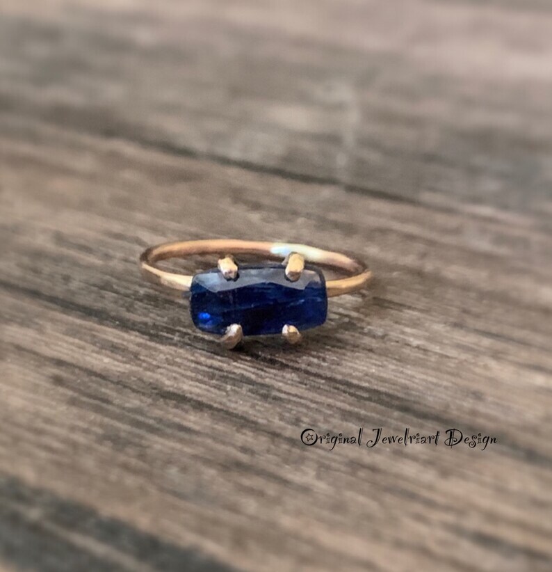 May include: A gold ring with a dark blue rectangular gemstone set in a prong setting.