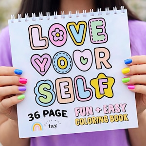 May include: A spiral-bound coloring book with the words "LOVE YOUR SELF" in colorful, outlined letters. The cover also includes the text "36 PAGE FUN + EASY COLORING BOOK" and a rainbow graphic. The book is held by a person with painted nails.