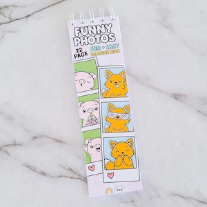May include: A spiral-bound 22-page coloring book titled FUNNY PHOTOS FUN + EASY COLORING BOOK. The cover features cartoon illustrations of a pig and a fox in photo booth strips, with a small rainbow logo and the text color with tay at the bottom.
