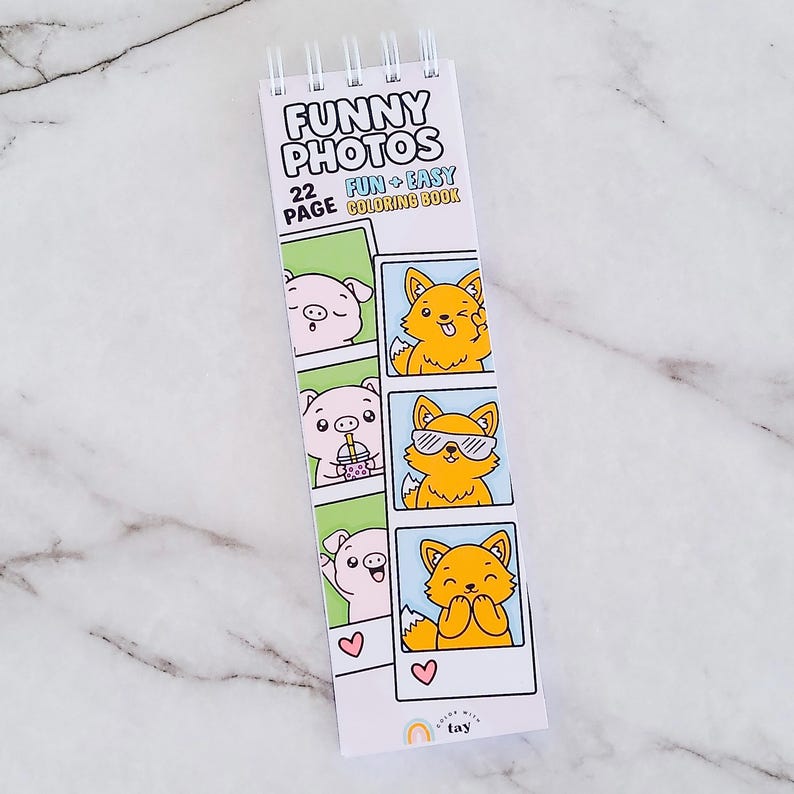 May include: A spiral-bound 22-page coloring book titled FUNNY PHOTOS FUN + EASY COLORING BOOK. The cover features cartoon illustrations of a pig and a fox in photo booth strips, with a small rainbow logo and the text color with tay at the bottom.