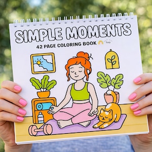 May include: A spiral-bound coloring book titled "SIMPLE MOMENTS" with a 42-page count. The cover features an illustration of a woman meditating, a cat, plants, and other wellness-themed images. The woman is wearing a green top and pink pants.
