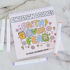 Peut inclure: Un livre de coloriage à spirales intitulé Christian Doodles avec le texte Faith Over Fear en lettres bulles colorées, entouré d'illustrations d'une Bible, de fleurs, de cœurs et de croix, accompagné de quatre marqueurs blancs sur les côtés.