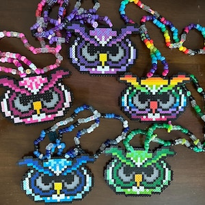 May include: Five colorful beaded necklaces with owl-shaped pixel art charms. The owls are purple, pink, rainbow, blue, and green.