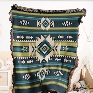 Könnte beinhalten: Eine gewebte Wolldecke mit einem geometrischen Muster in Blautönen, Grün- und Weißtönen. Die Decke hat einen Fransenrand und zeigt ein stilisiertes Schildkrötenmotiv.