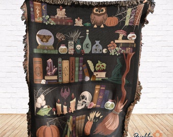 May include: A black and brown woven tapestry throw blanket with a whimsical design featuring a bookshelf filled with books, potions, crystals, candles, a skull, a broom, a frog, an owl, and pumpkins. The design is set against a dark background with a spiderweb and other magical elements.