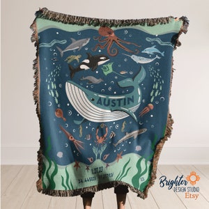 May include: A blue woven throw blanket with a personalized name "Austin" in the center. The blanket features a whale, octopus, seahorse, starfish, and other sea creatures on a blue background with green seaweed.