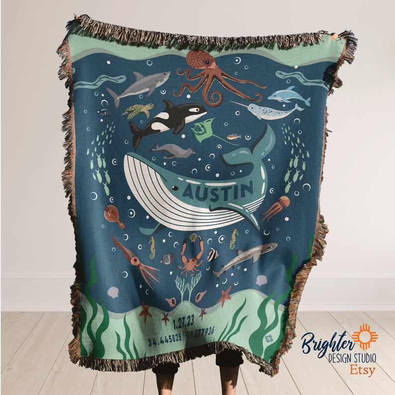 May include: A blue woven throw blanket with a personalized name "Austin" in the center. The blanket features a whale, octopus, seahorse, starfish, and other sea creatures on a blue background with green seaweed.
