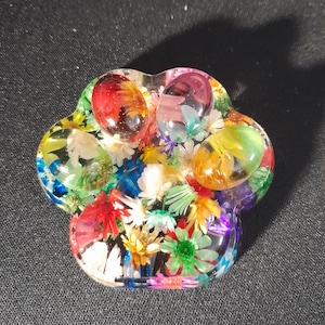 May include: A colourful paw print shaped resin paperweight with embedded pressed flowers and clear resin. The paw print is filled with a variety of flowers in shades of red, yellow, green, blue, and white.
