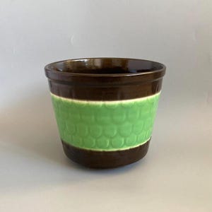 May include: A ceramic planter featuring a glossy dark brown rim and base with a wide, textured band of light green in the centre. The green section displays a repeating embossed scale pattern that wraps around the exterior of the round vessel.