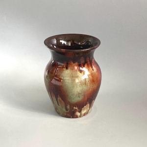 May include: A ceramic vase with a wide, flared rim and a rounded body. The surface features a glossy glaze with a blended colour palette of deep chocolate brown, warm amber, and creamy off-white, creating a fluid, dripping effect throughout.