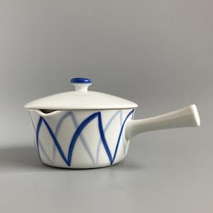 May include: White ceramic soup bowl with a lid and handle. The bowl has a blue geometric pattern and a blue knob on the lid. The handle is white and extends from the side of the bowl.