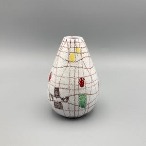 May include: A white ceramic vase with a teardrop shape and a brown, red, yellow, and green geometric pattern.