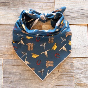May include: A blue bandana with a white trim featuring a pattern of cowboy boots, horseshoes, and hats.